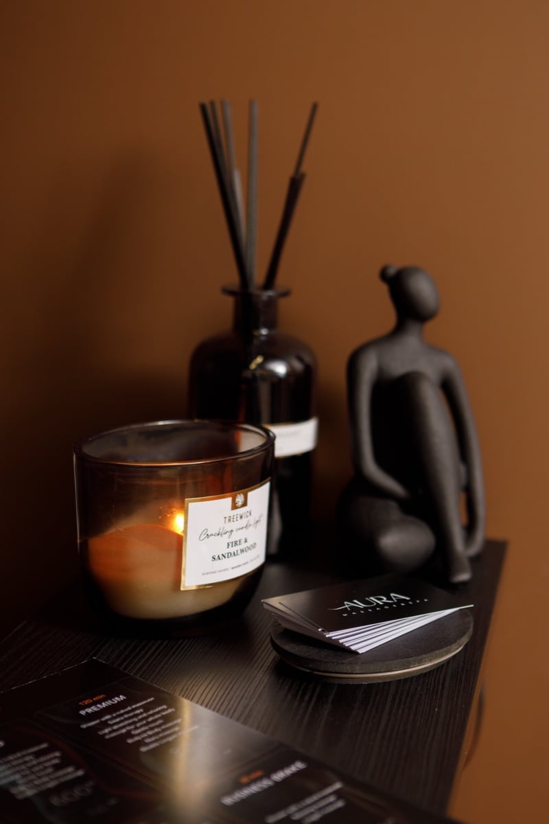 A lit candle, a reed diffuser and a figurine on a table beside the salon's cards