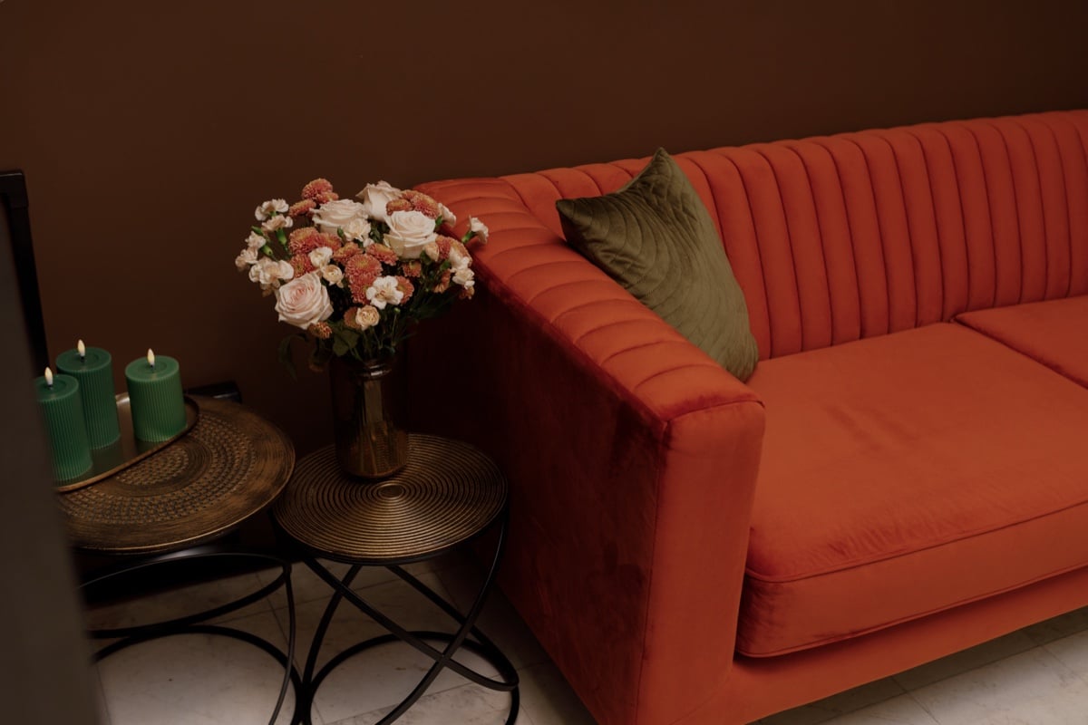 Lounge corner: a velvet sofa, a bouquet of roses and green candles on brass tables
